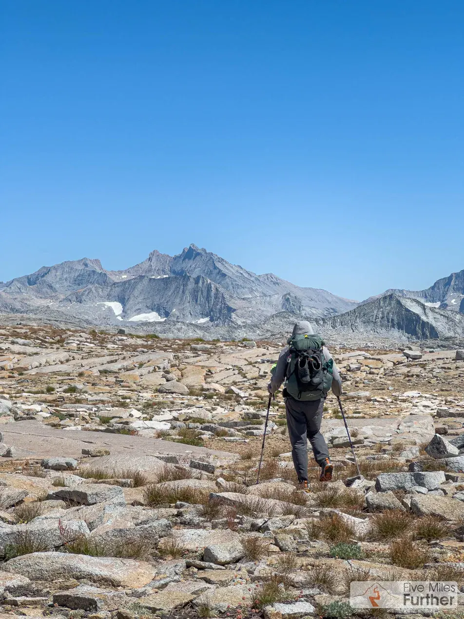 Backpacker crossing a granite boulder field toward high peaks