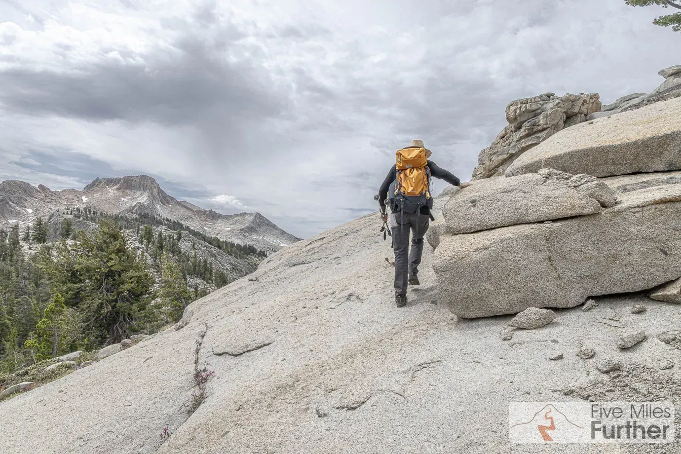 Backpacker scrambling up a granite ledge under building storm clouds